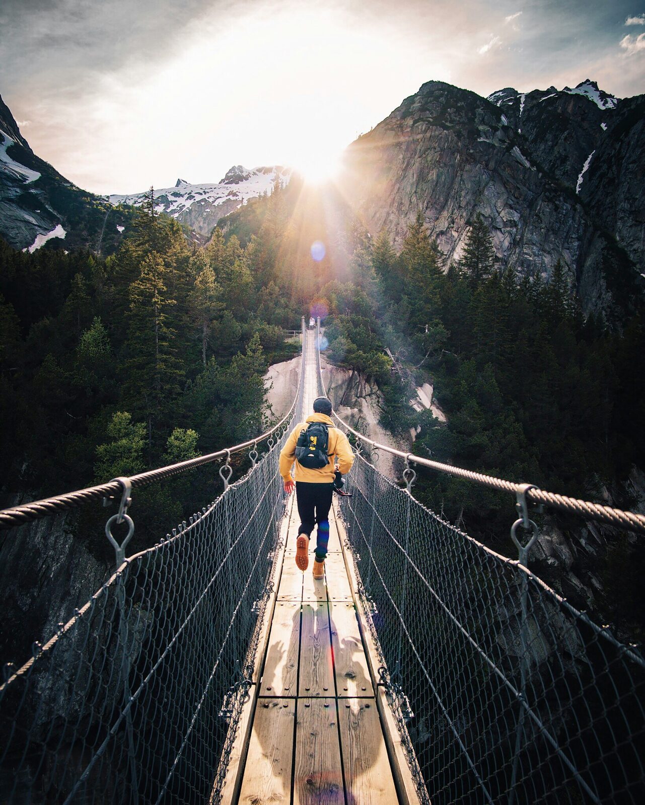 Randonneur sur un pont suspendu en montagne, sac à dos technique